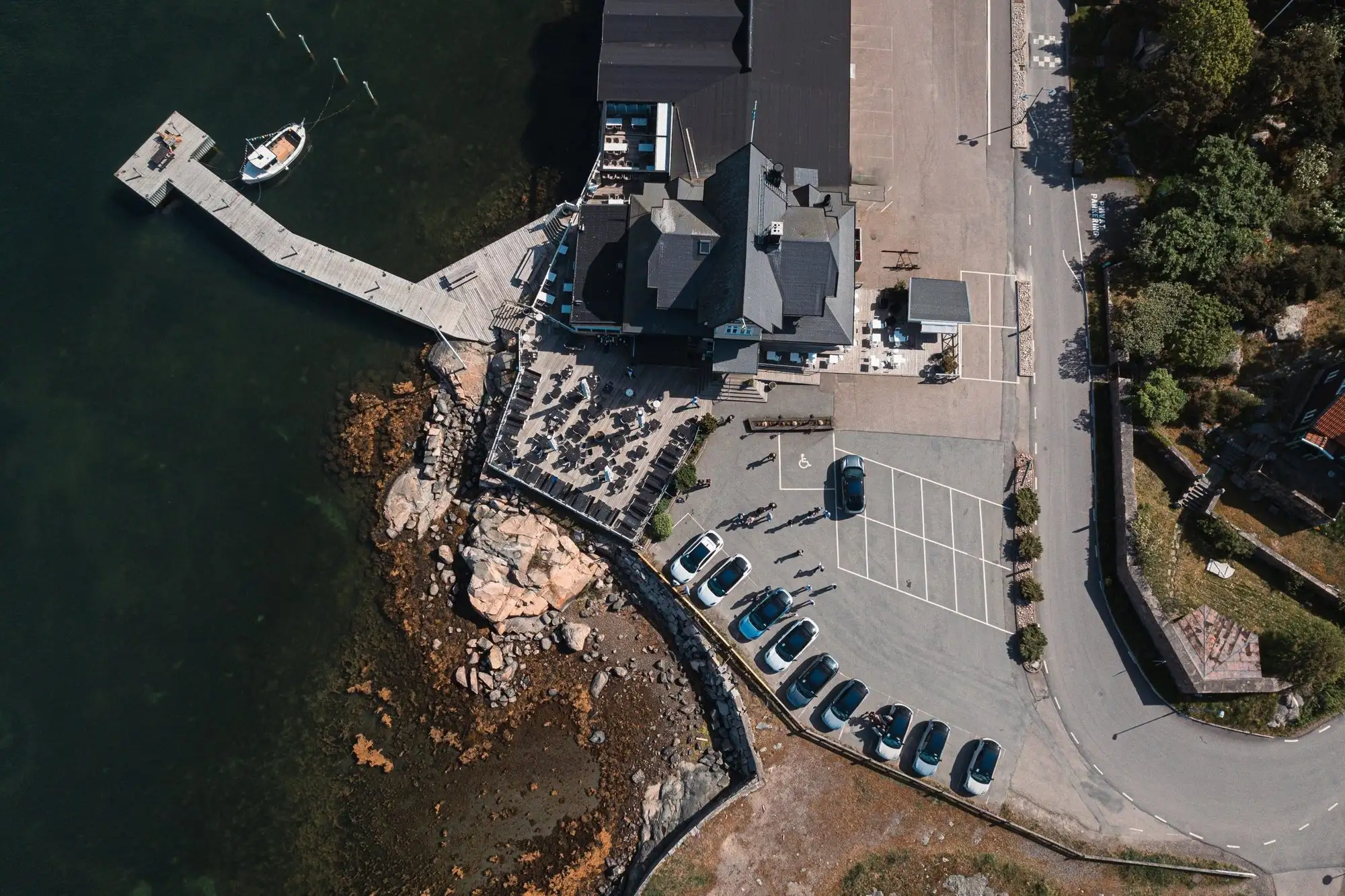 Flygbild över en kuststräcka med brygga, byggnader och parkering