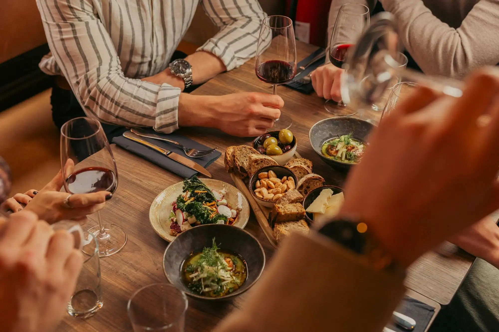Gäster delar rätter och vin vid ett träbord