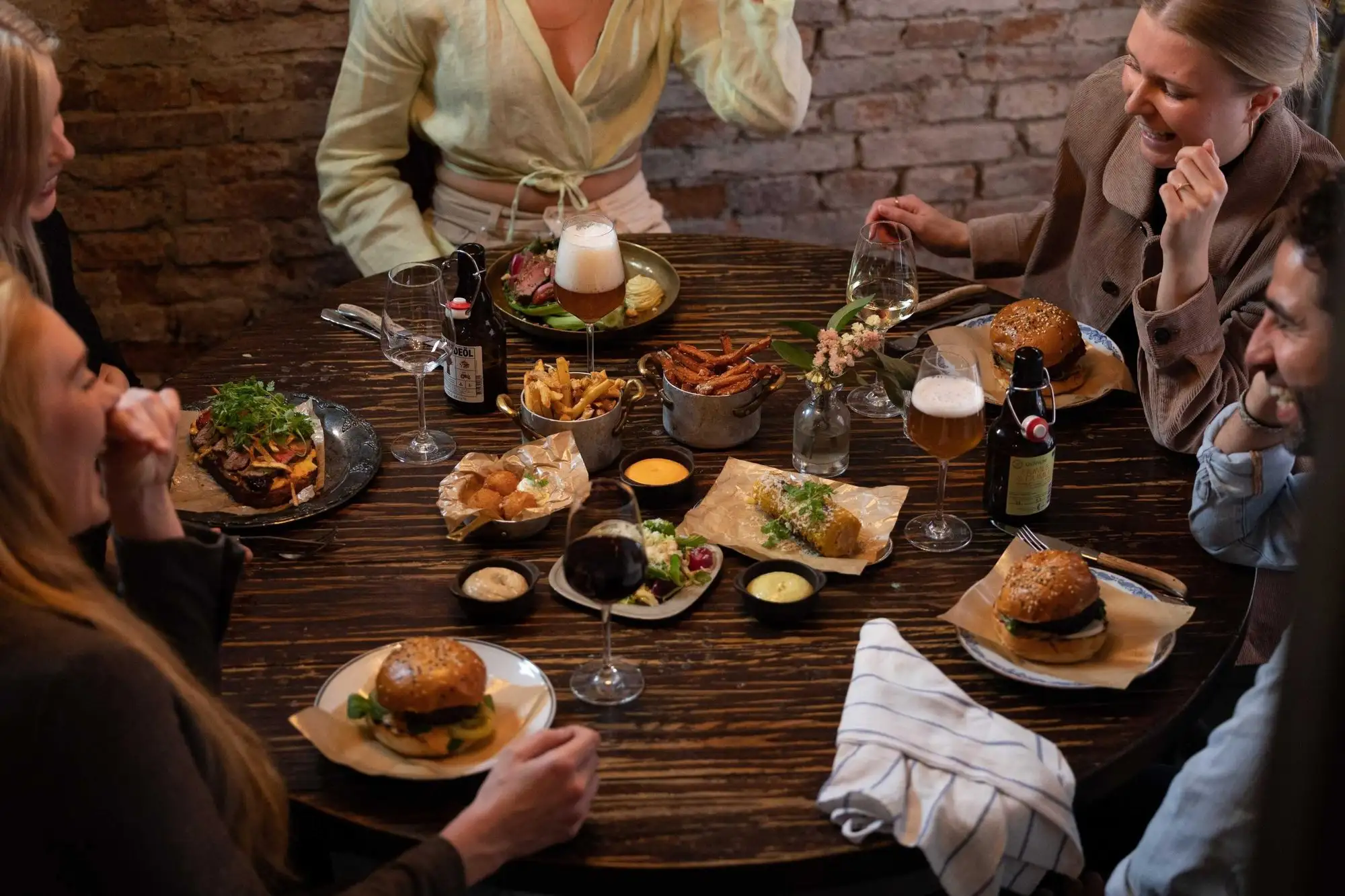 Restaurangbord fullt av rätter och dryck med gäster runt omkring