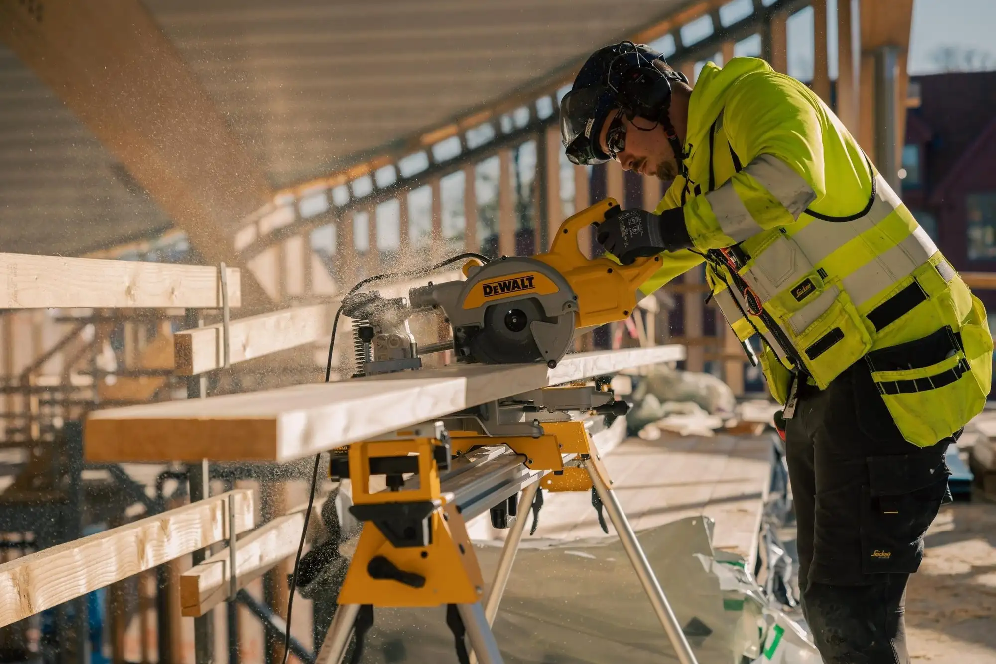 Byggarbetare i varselkläder sågar en bräda på en byggplats