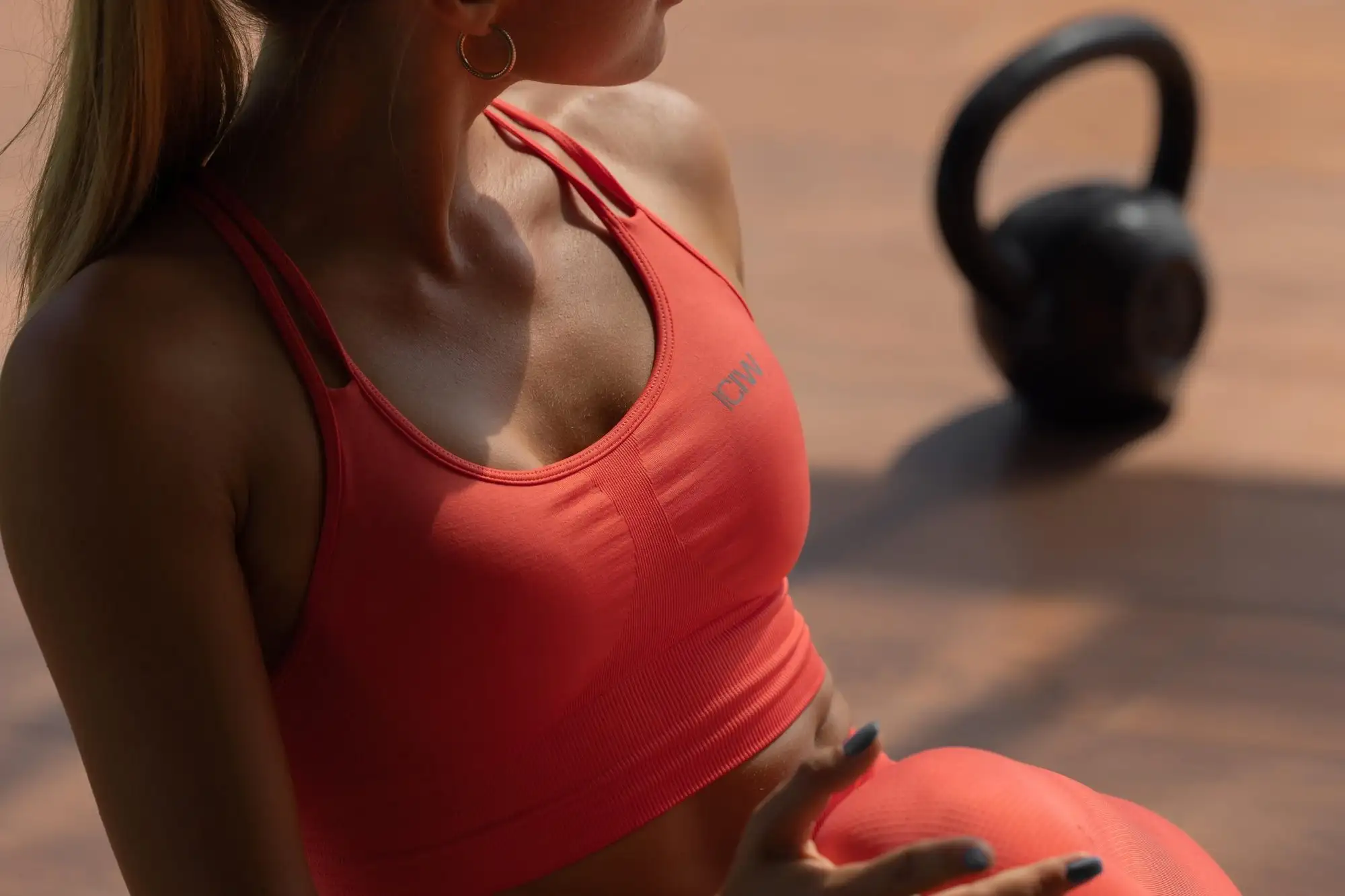 Närbild på kvinna i röd träningstopp med en kettlebell i bakgrunden